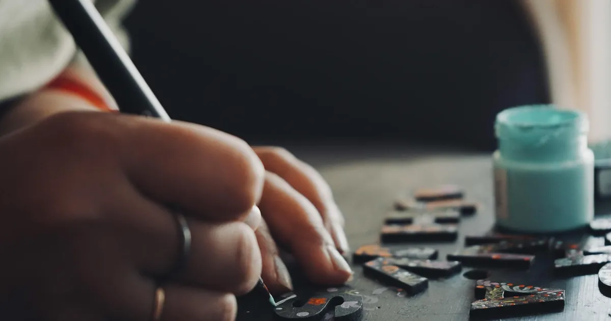 Detailed view of a hand using a brush to paint puzzle pieces, showcasing artistic creativity and precision. Detailed view of a hand using a brush to paint puzzle pieces, showcasing artistic creativity and precision.