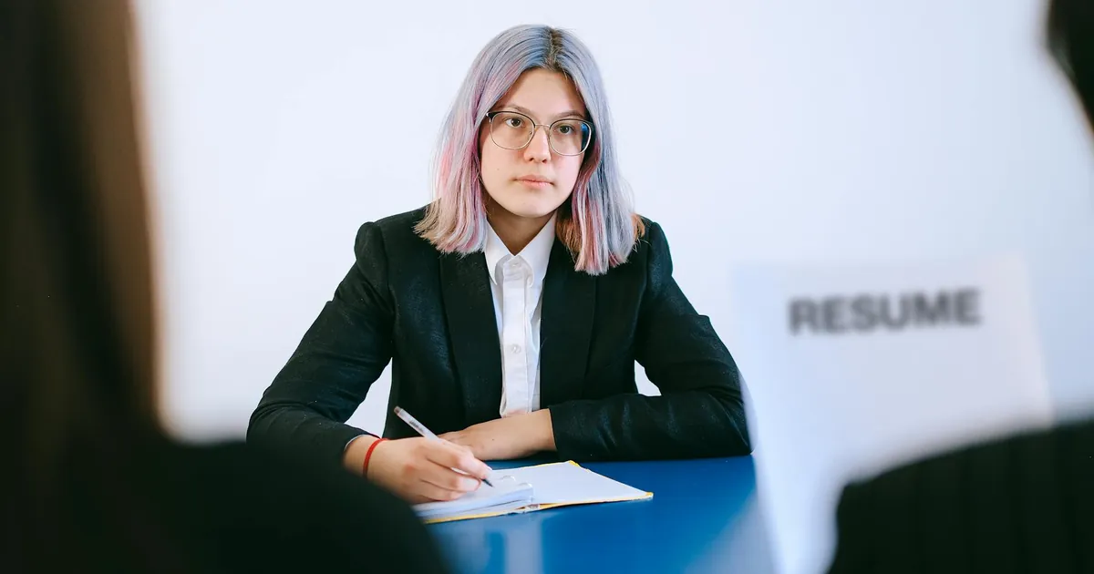 A young woman in a suit during a job interview, writing notes.
