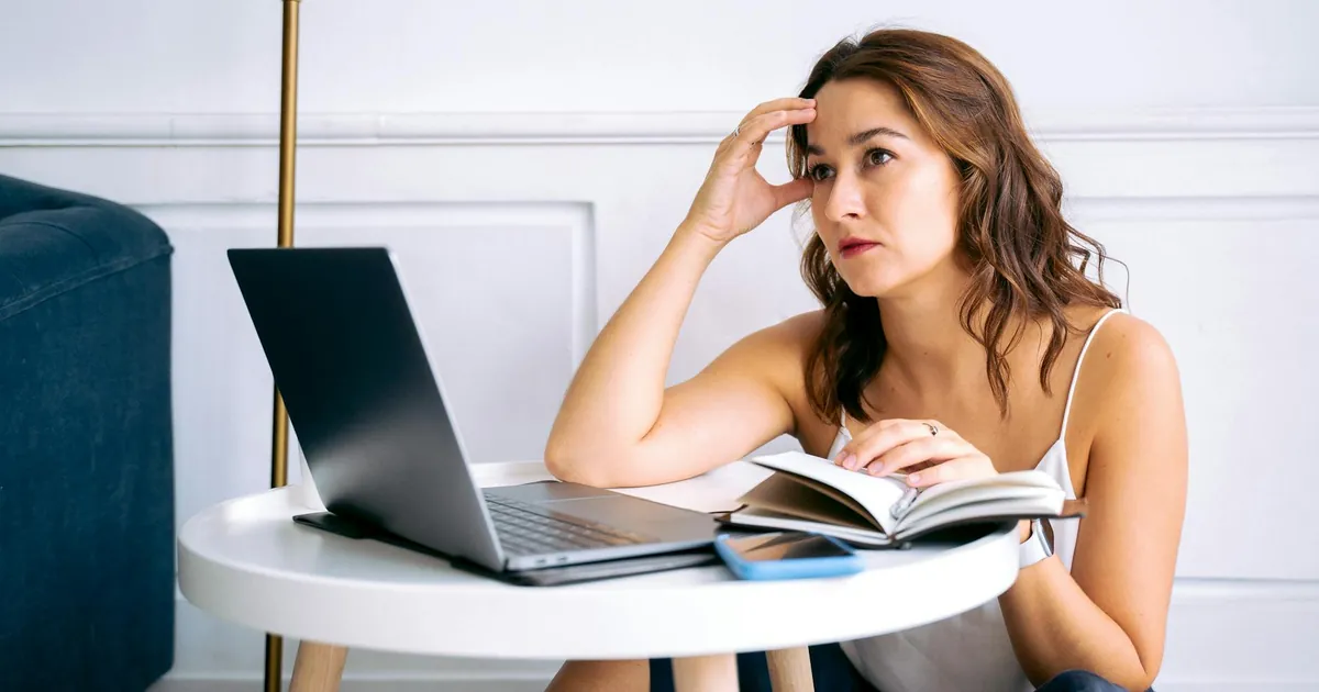 A stressed woman sitting at a desk with a laptop and notebook, reflecting work burnout.