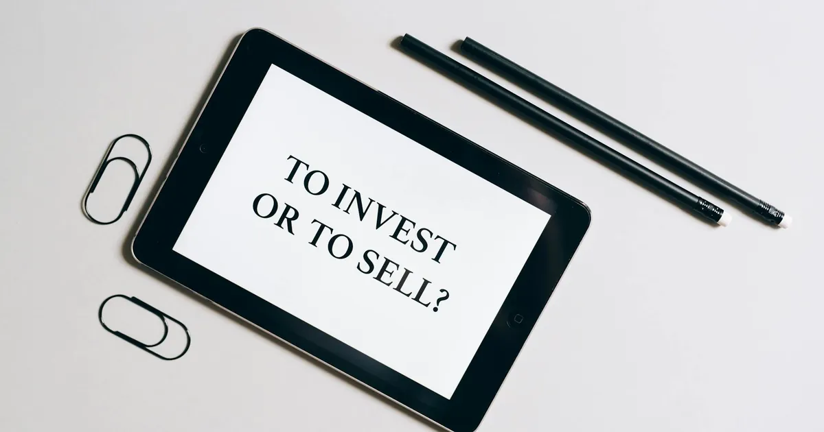 Flat lay of tablet with investment decision text, surrounded by stationery on a white table.