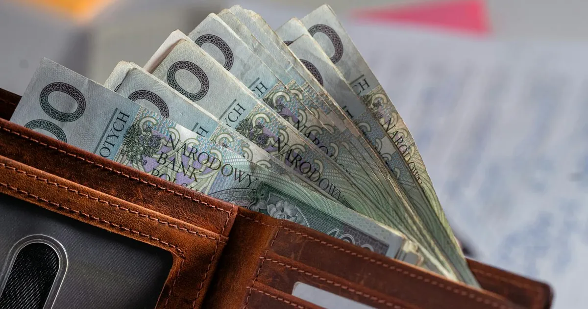 Brown leather wallet containing Polish zloty banknotes on cluttered desk