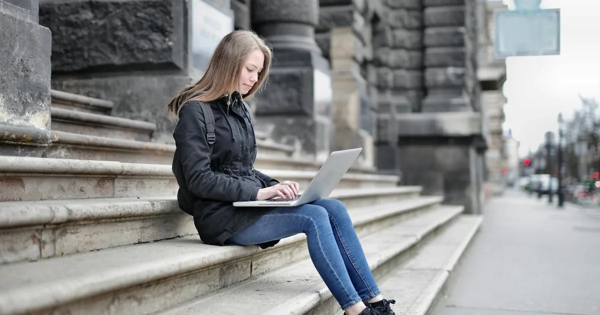 Woman using laptop seated on historic building steps for remote work.