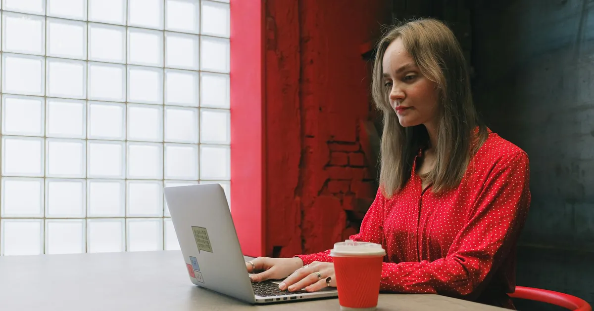 Woman in red blouse focused on work with laptop and coffee indoors. Woman in red blouse focused on work with laptop and coffee indoors.