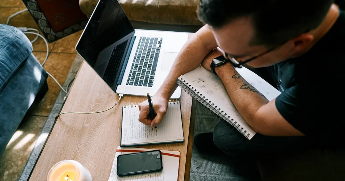 man in black t-shirt writing on white paper