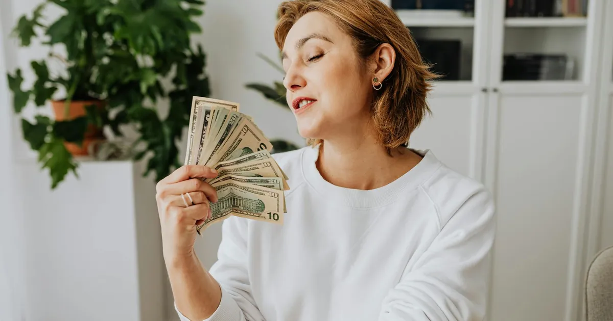 Woman holding US dollars in a relaxed indoor setting, reflecting satisfaction and success.