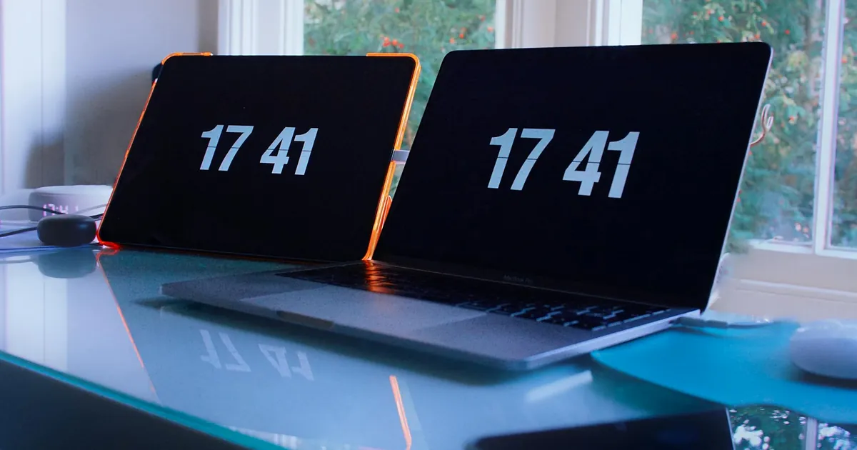 Laptops showing time 17:41 on glass desk, bright workspace.
