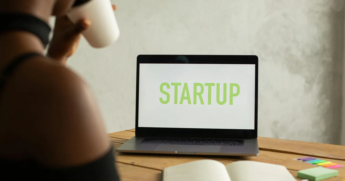 An entrepreneur in a workspace with a laptop displaying 'STARTUP', sipping coffee.
