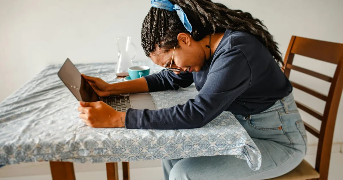 Young woman with laptop looking stressed and tired at home, expressing work frustration.