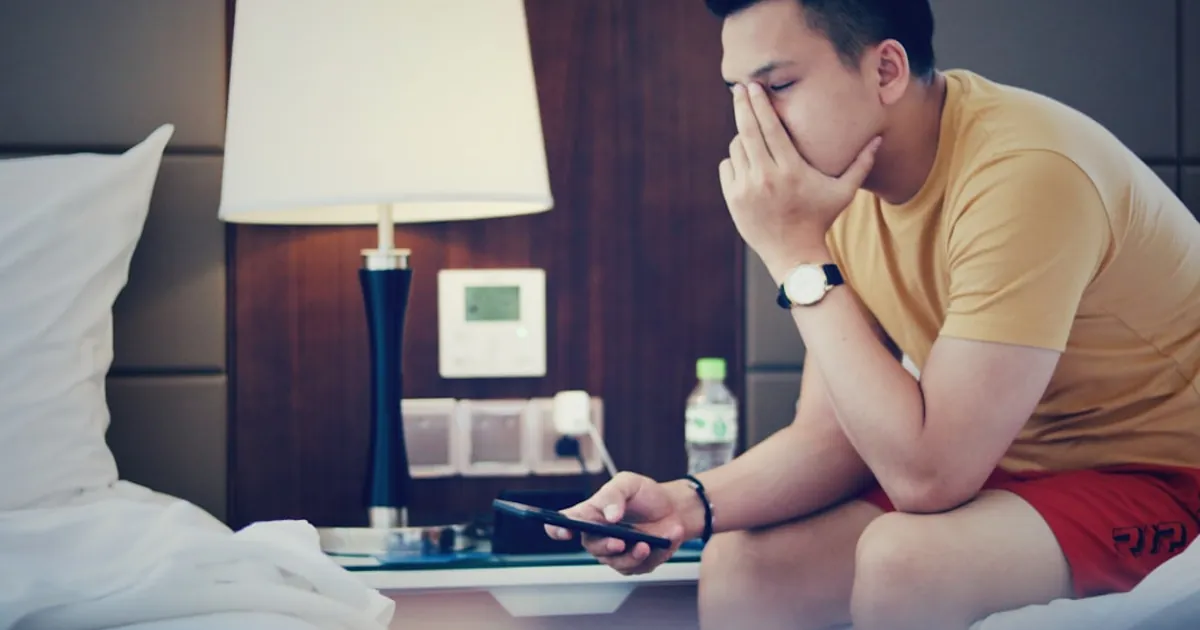man holding phone and sitting while putting left hand on his face