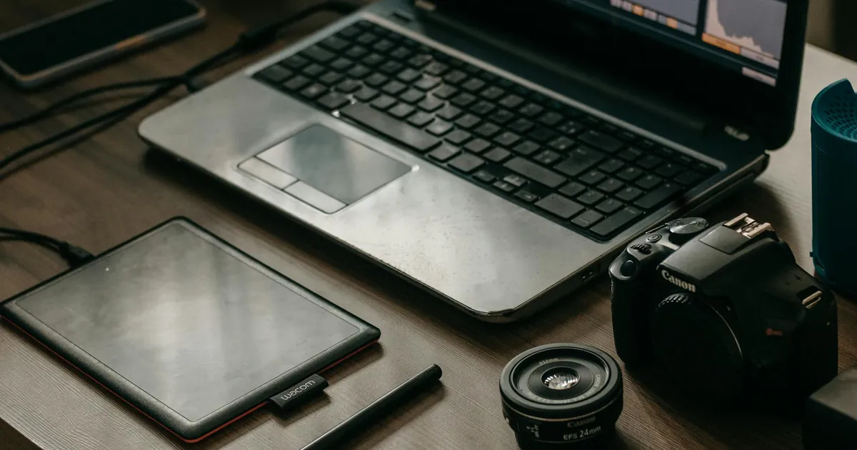 Laptop, camera, lens, and graphic tablet on a desk for digital creatives.