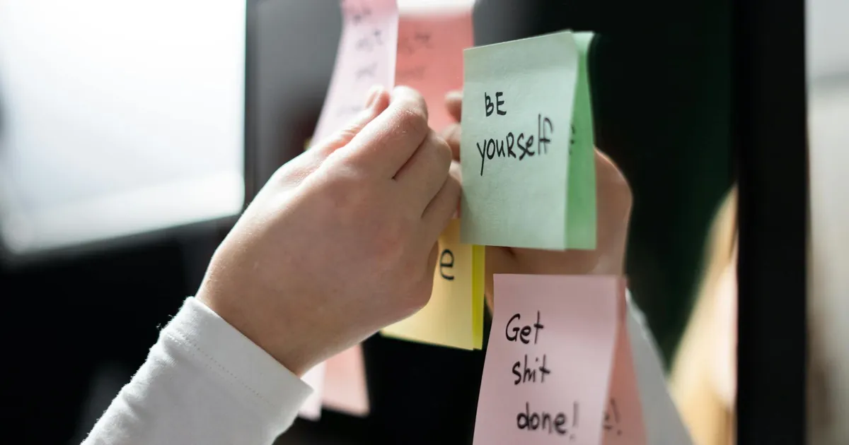 Close-up of hand placing colorful motivational sticky notes on a mirror, inspiring messages. Close-up of hand placing colorful motivational sticky notes on a mirror, inspiring messages.