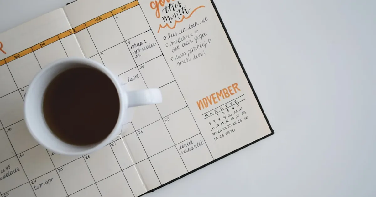 white ceramic mug with coffee on top of a planner white ceramic mug with coffee on top of a planner