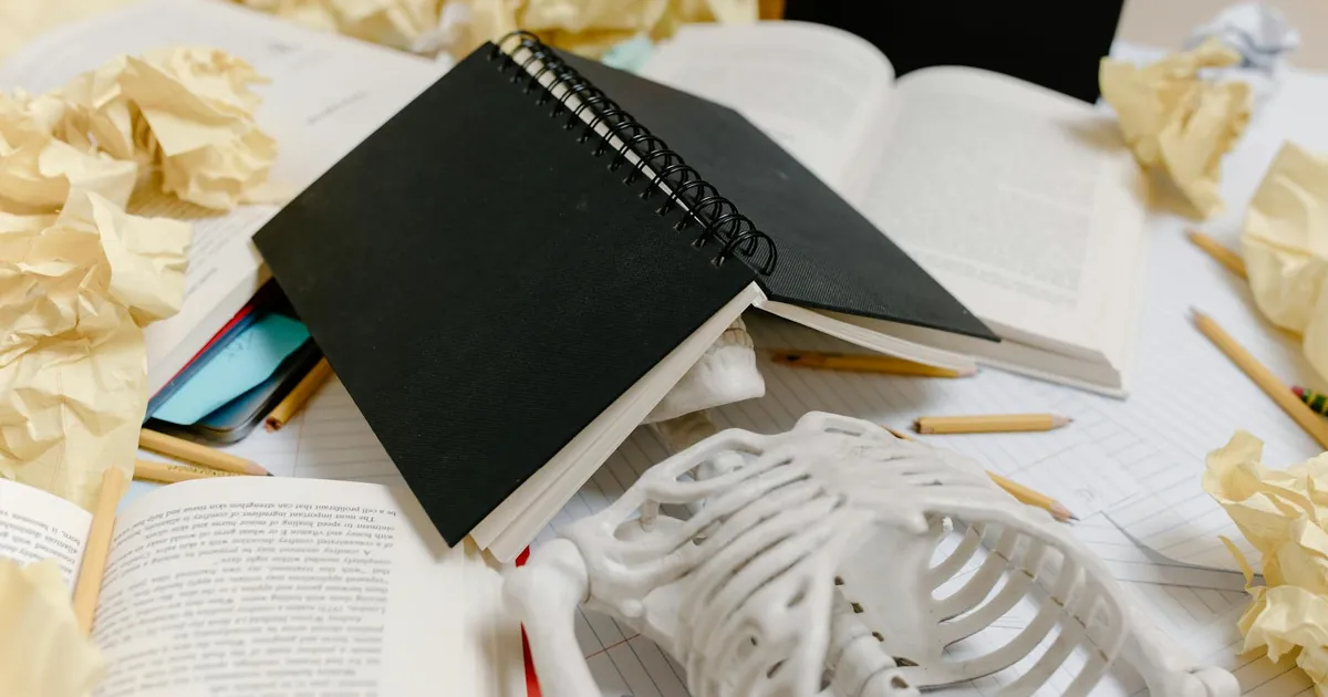 A symbolic display of academic burnout with a notebook, skeleton, and crumpled papers.