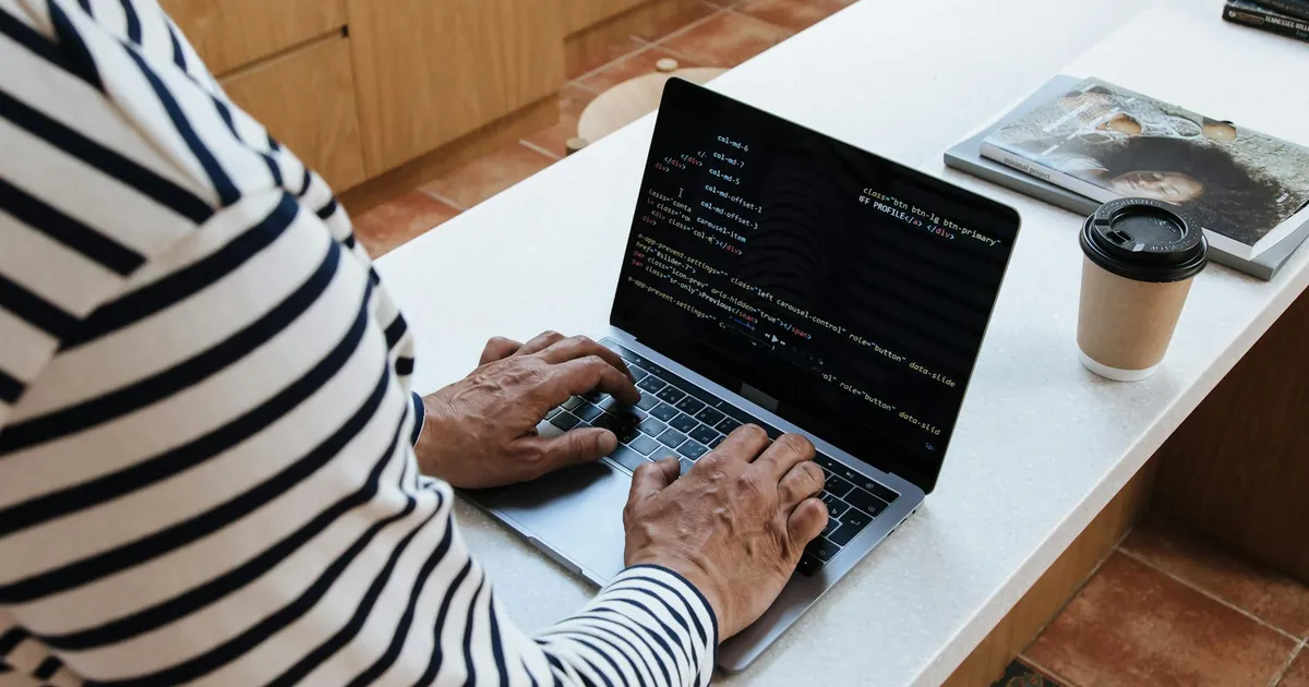 A senior adult programmer coding at home on a laptop, showcasing a work-from-home setup.