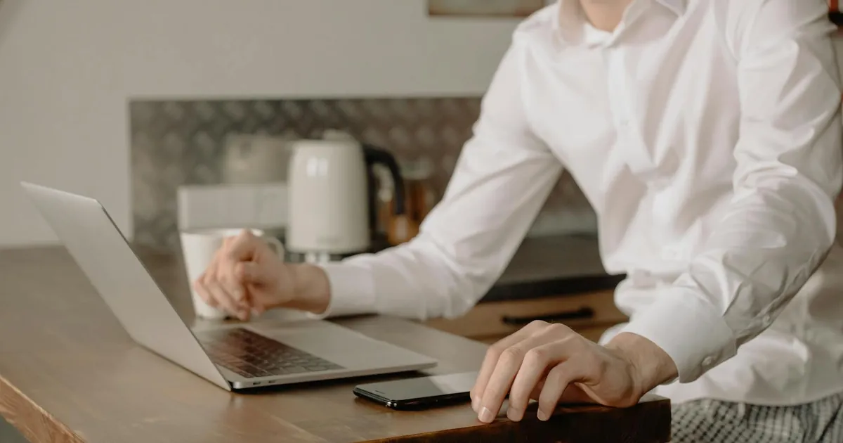 A man in casual attire works on a laptop in his kitchen, embracing remote work life.